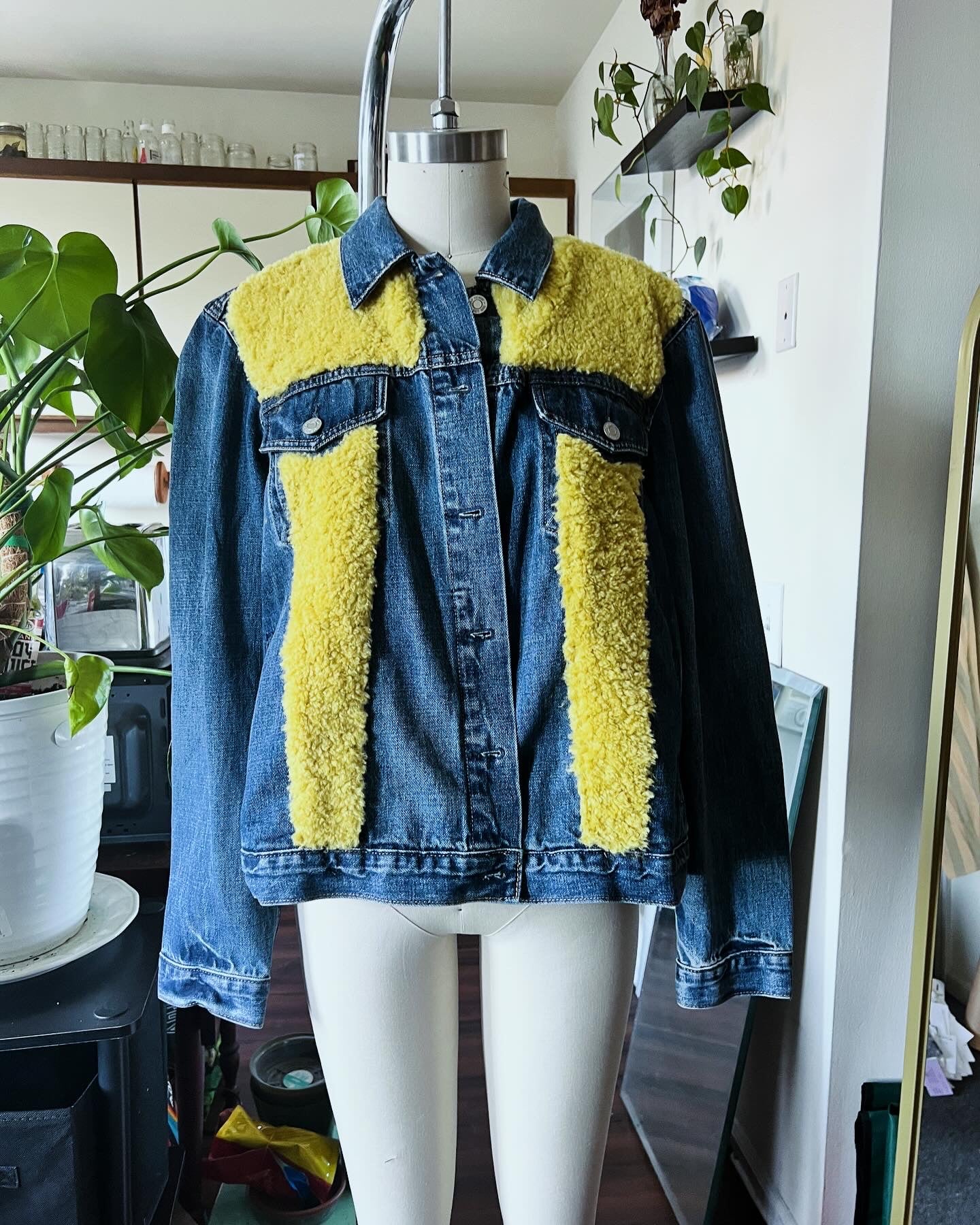 A denim jacket with yellow accents on the upper part, displayed on a mannequin in a studio setting.