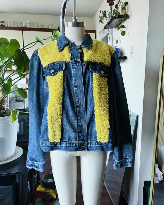 A denim jacket with yellow accents on the upper part, displayed on a mannequin in a studio setting.