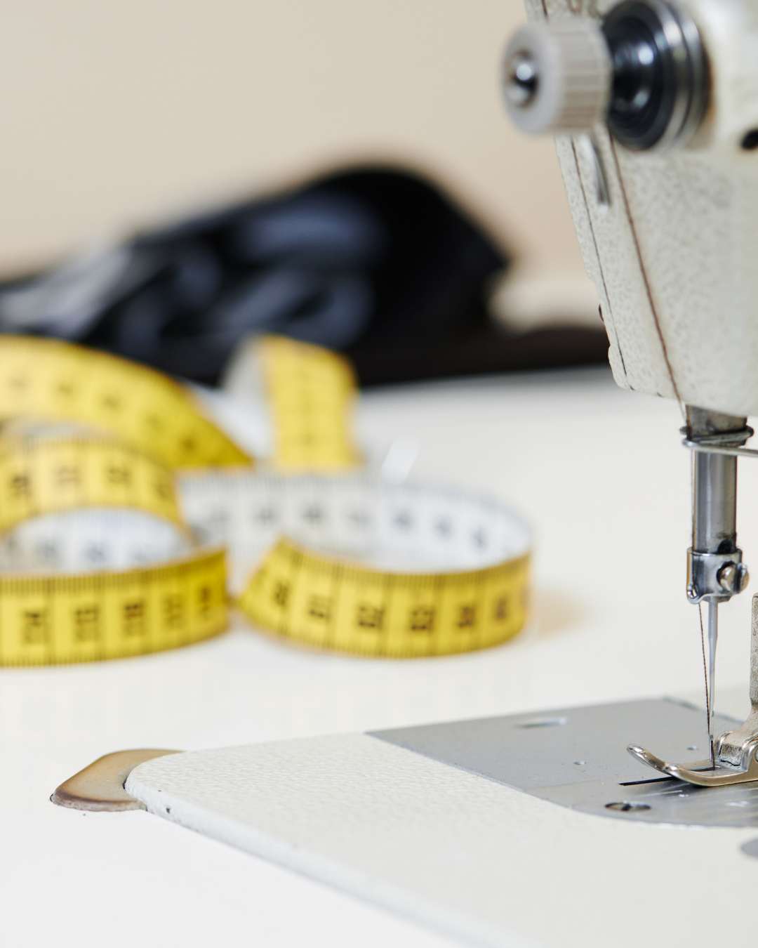 A sewing machine needle in focus with a measuring tape and fabric in the background, indicating a sewing-related activity.