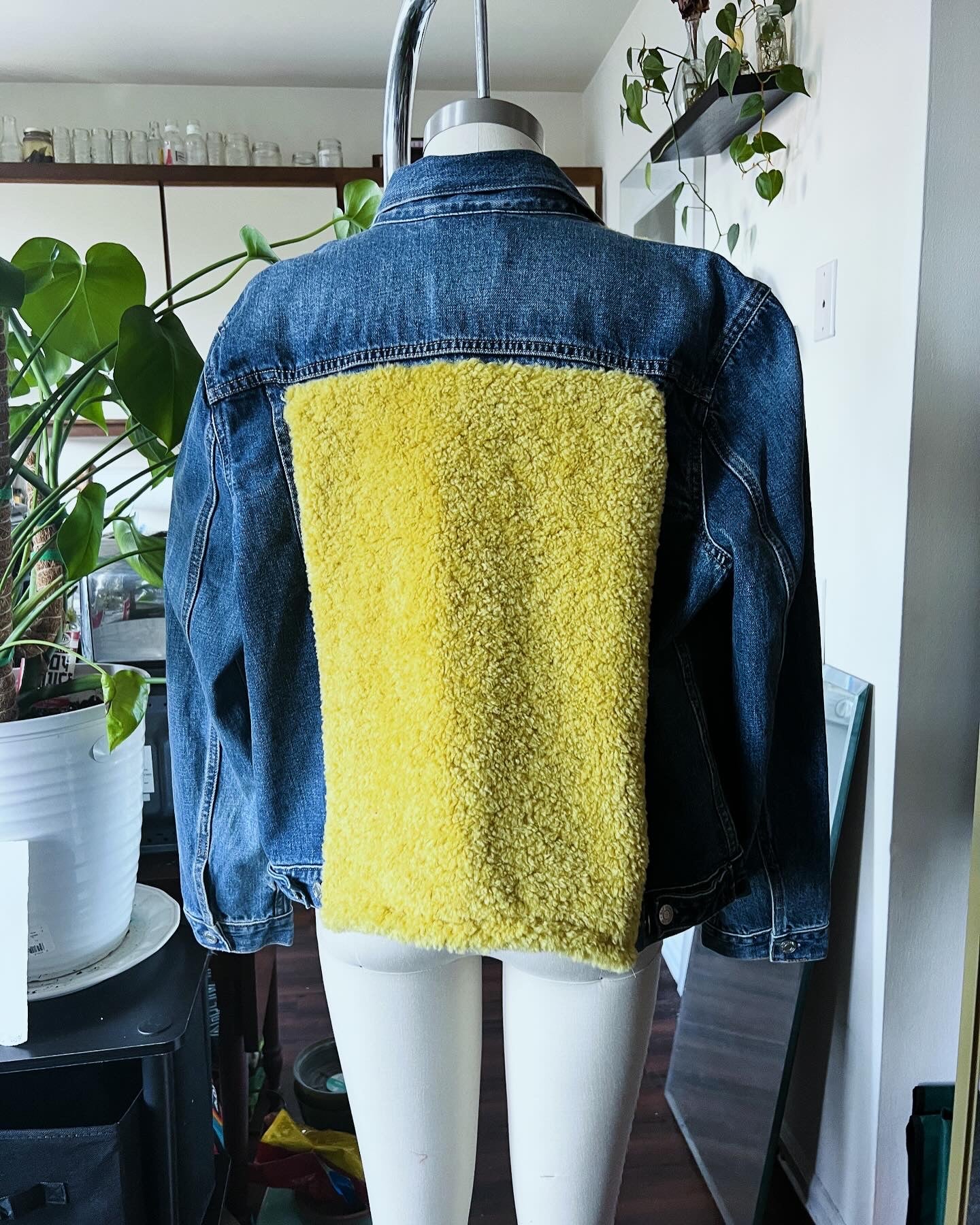 A denim jacket with yellow accents on the upper part, displayed on a mannequin in a studio setting.