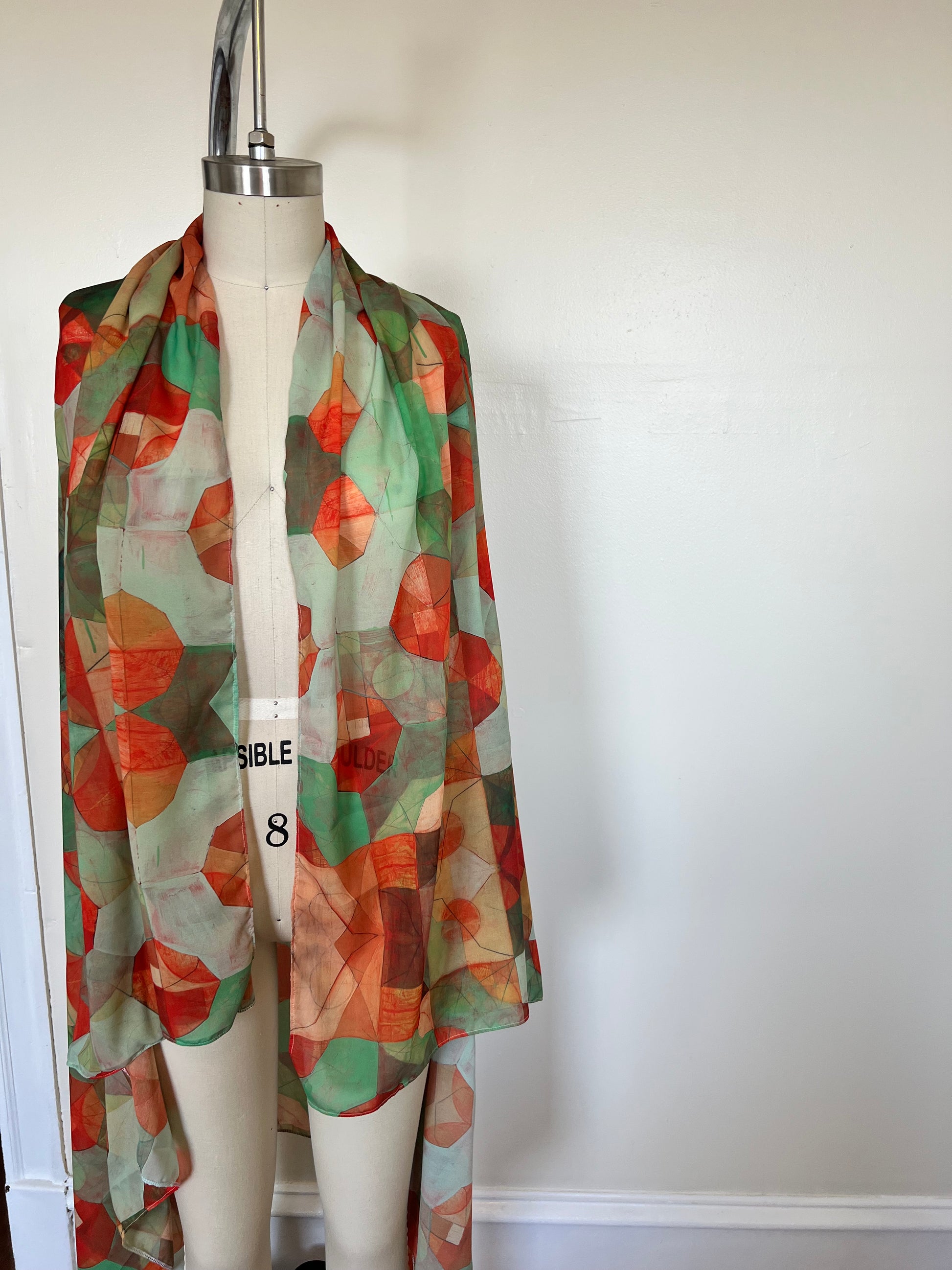A large chiffon silk scarf with a vibrant, abstract multicolored print, displayed on a mannequin.