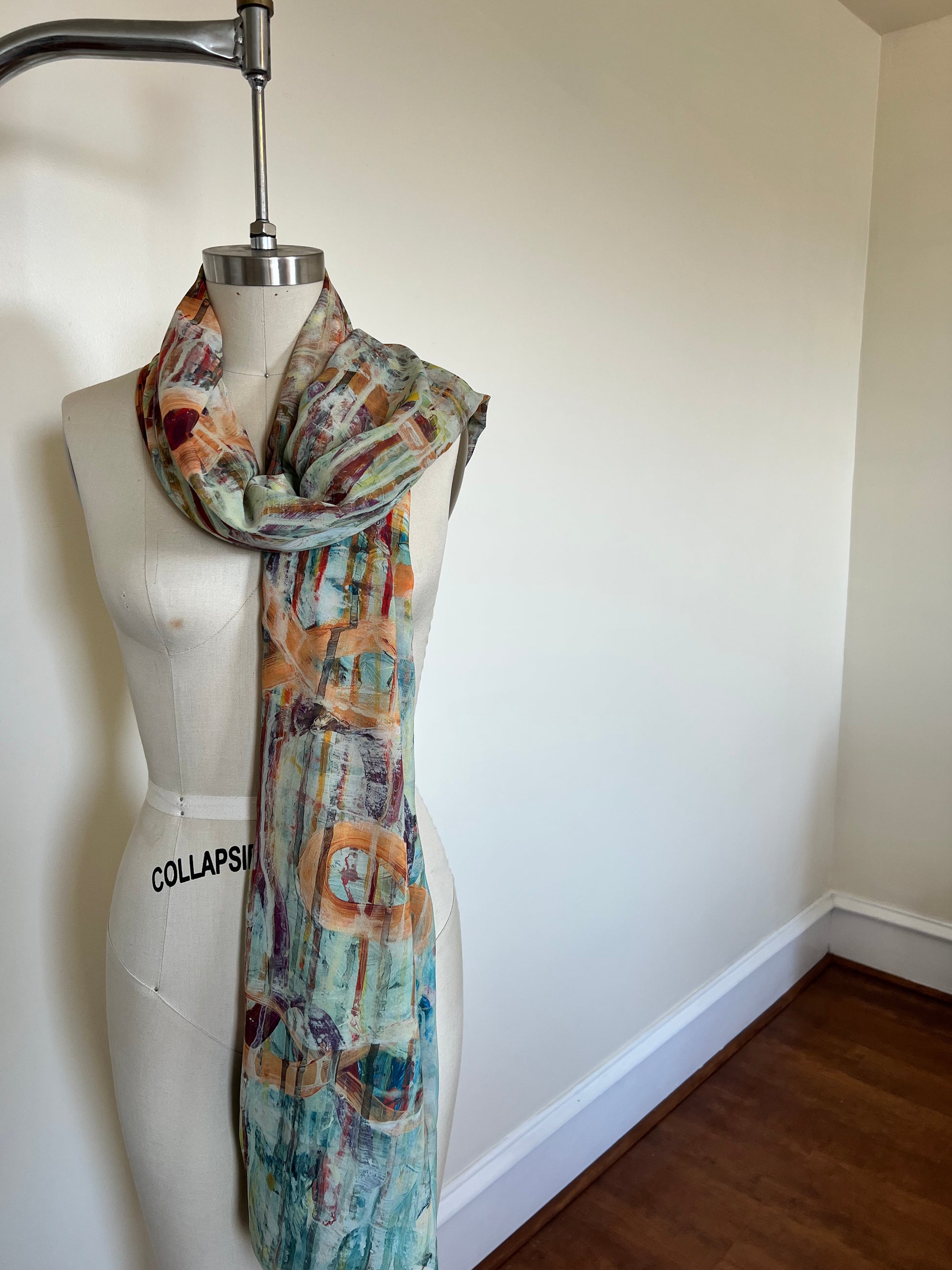 A large chiffon silk scarf with a vibrant, abstract multicolored print, displayed on a mannequin.
