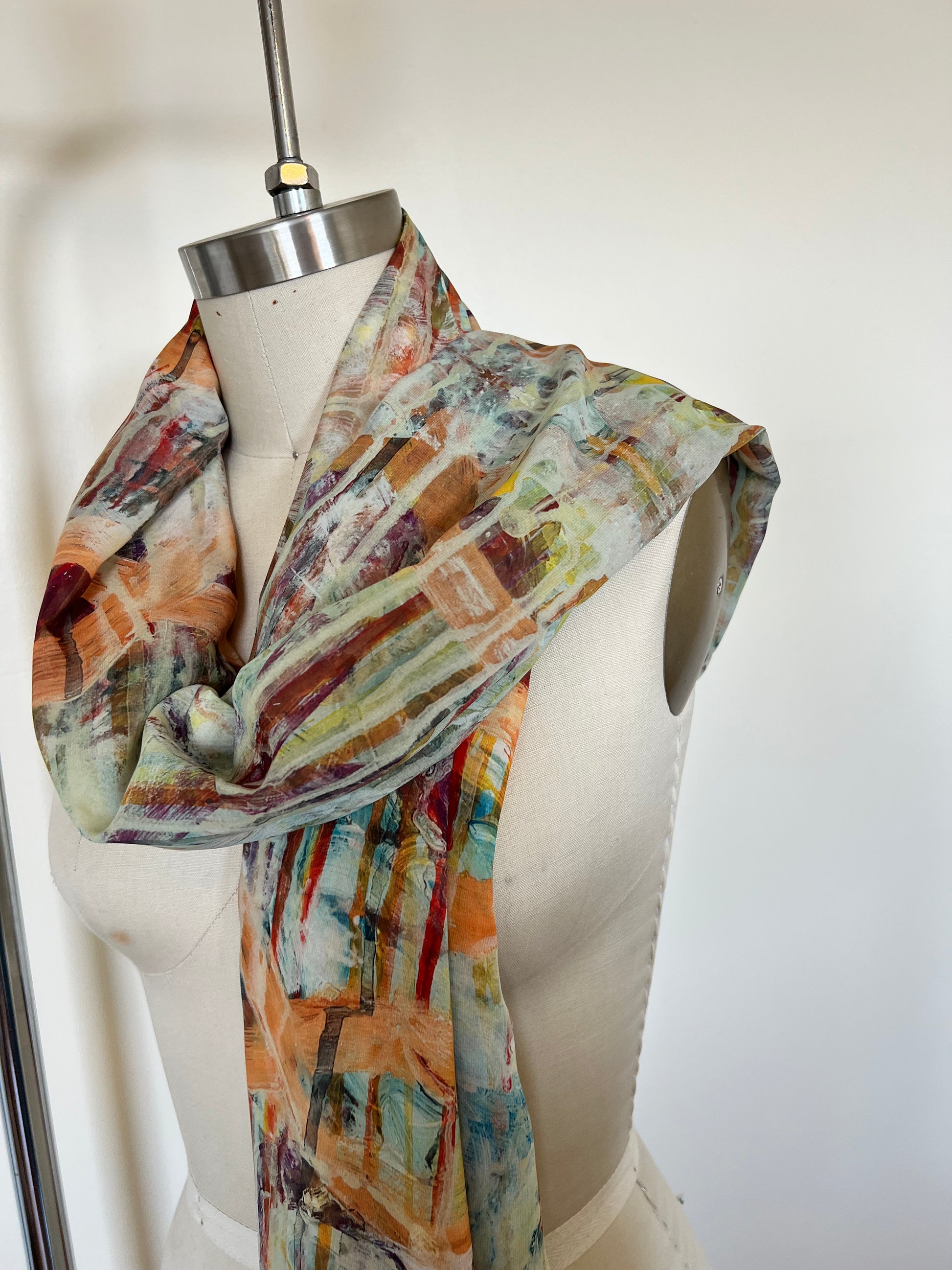 A large chiffon silk scarf with a vibrant, abstract multicolored print, displayed on a mannequin.