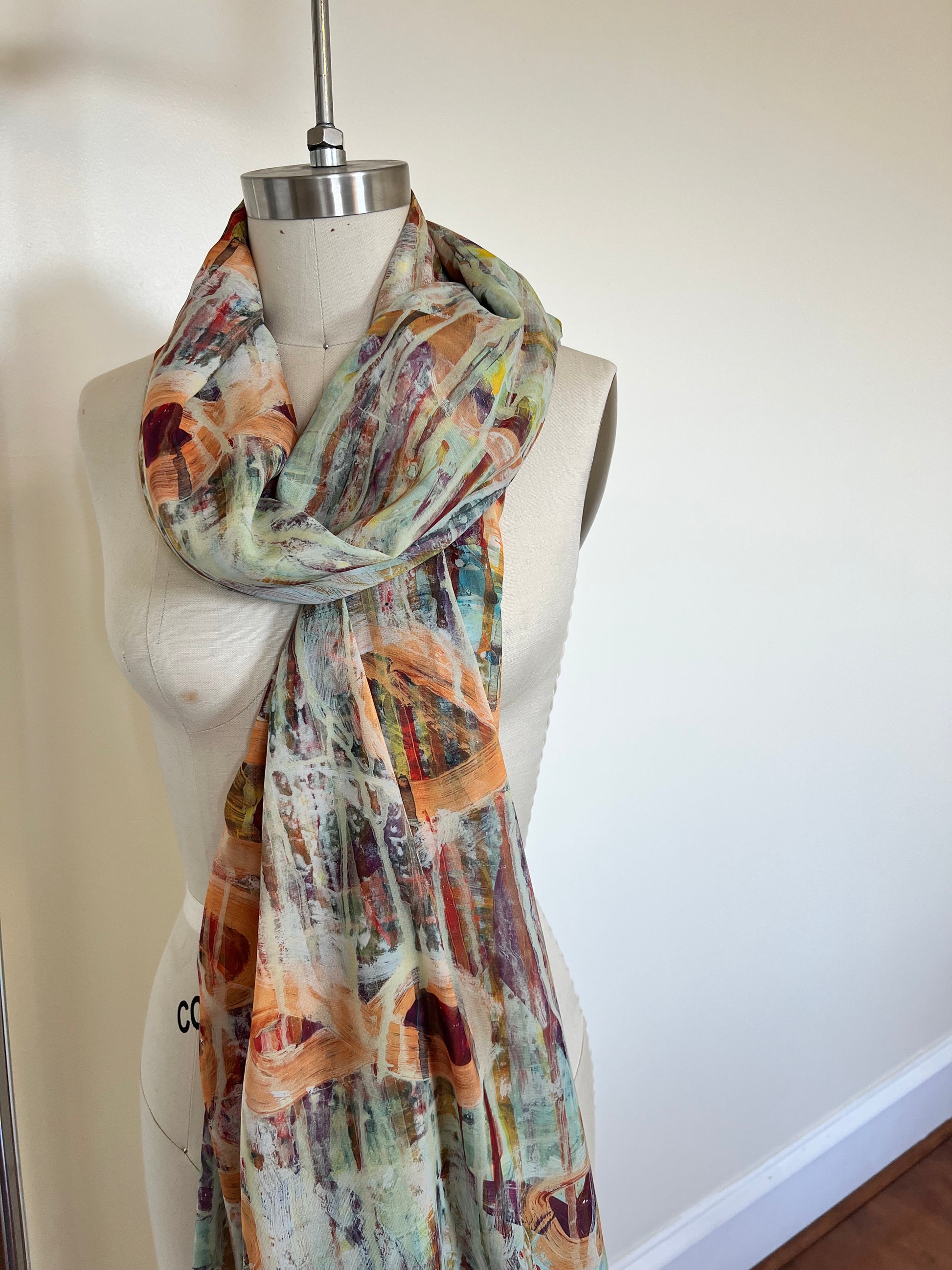 A large chiffon silk scarf with a vibrant, abstract multicolored print, displayed on a mannequin.