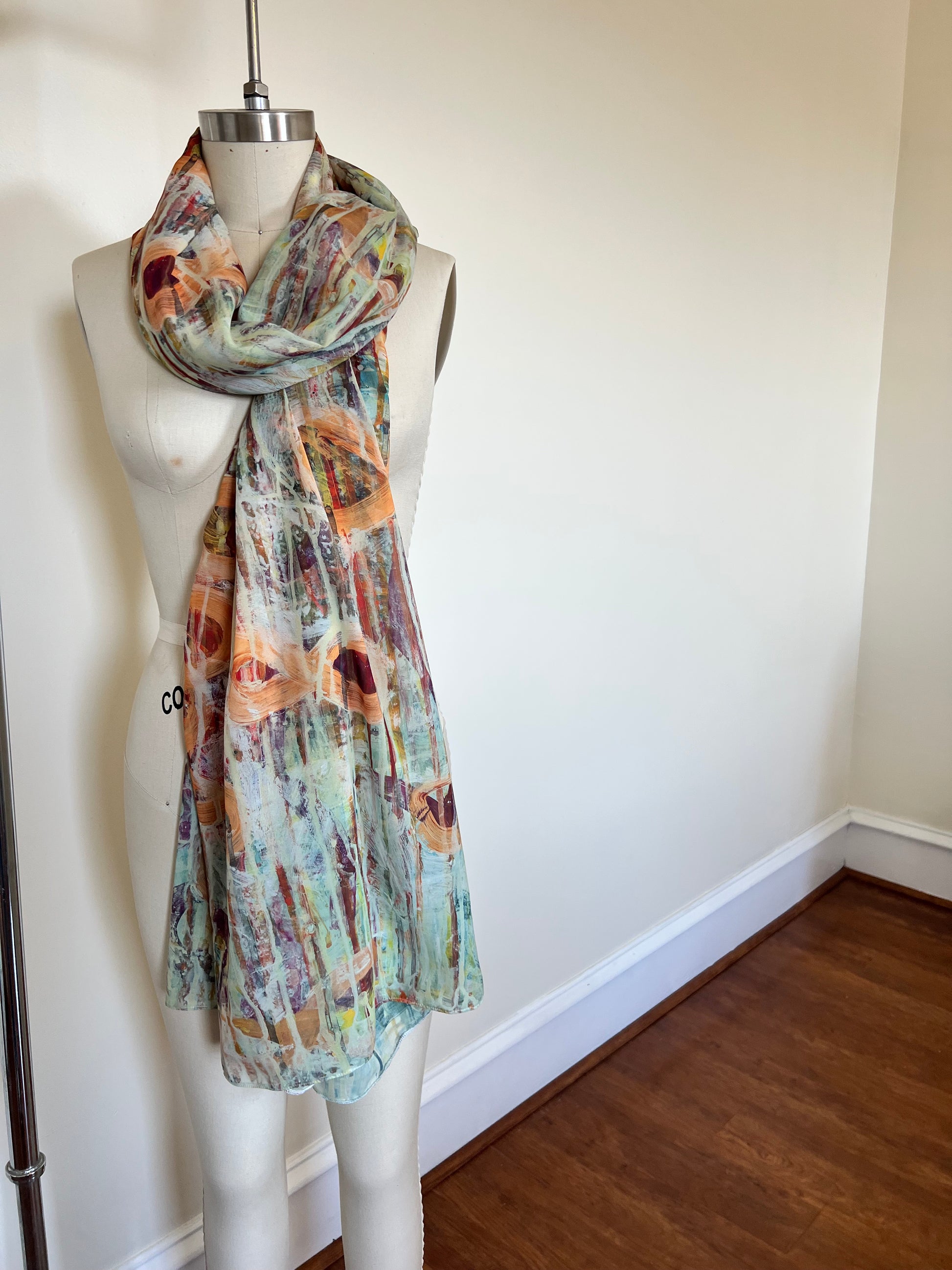 A large chiffon silk scarf with a vibrant, abstract multicolored print, displayed on a mannequin.