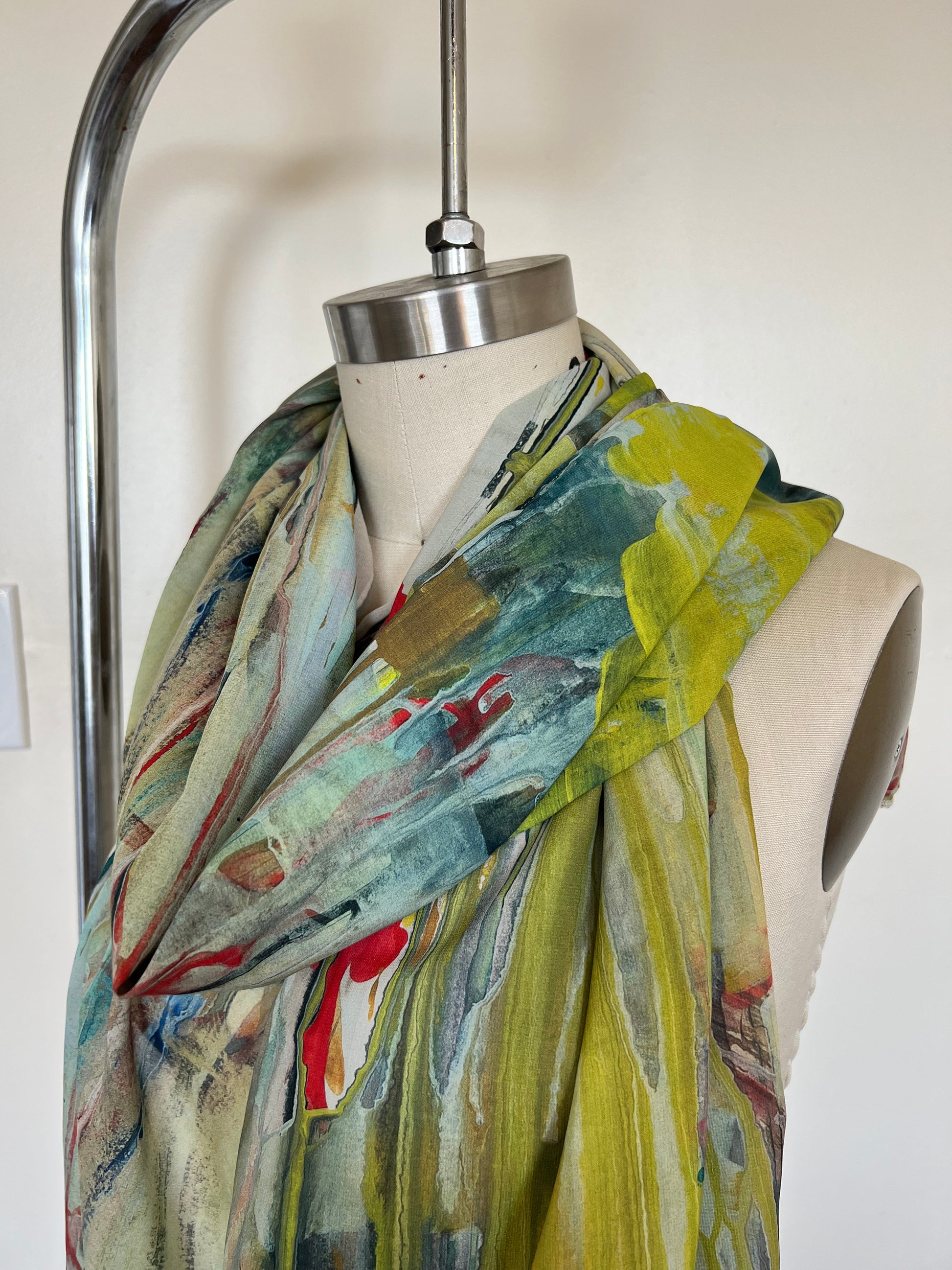 A large chiffon silk scarf with a vibrant, abstract multicolored print, displayed on a mannequin.