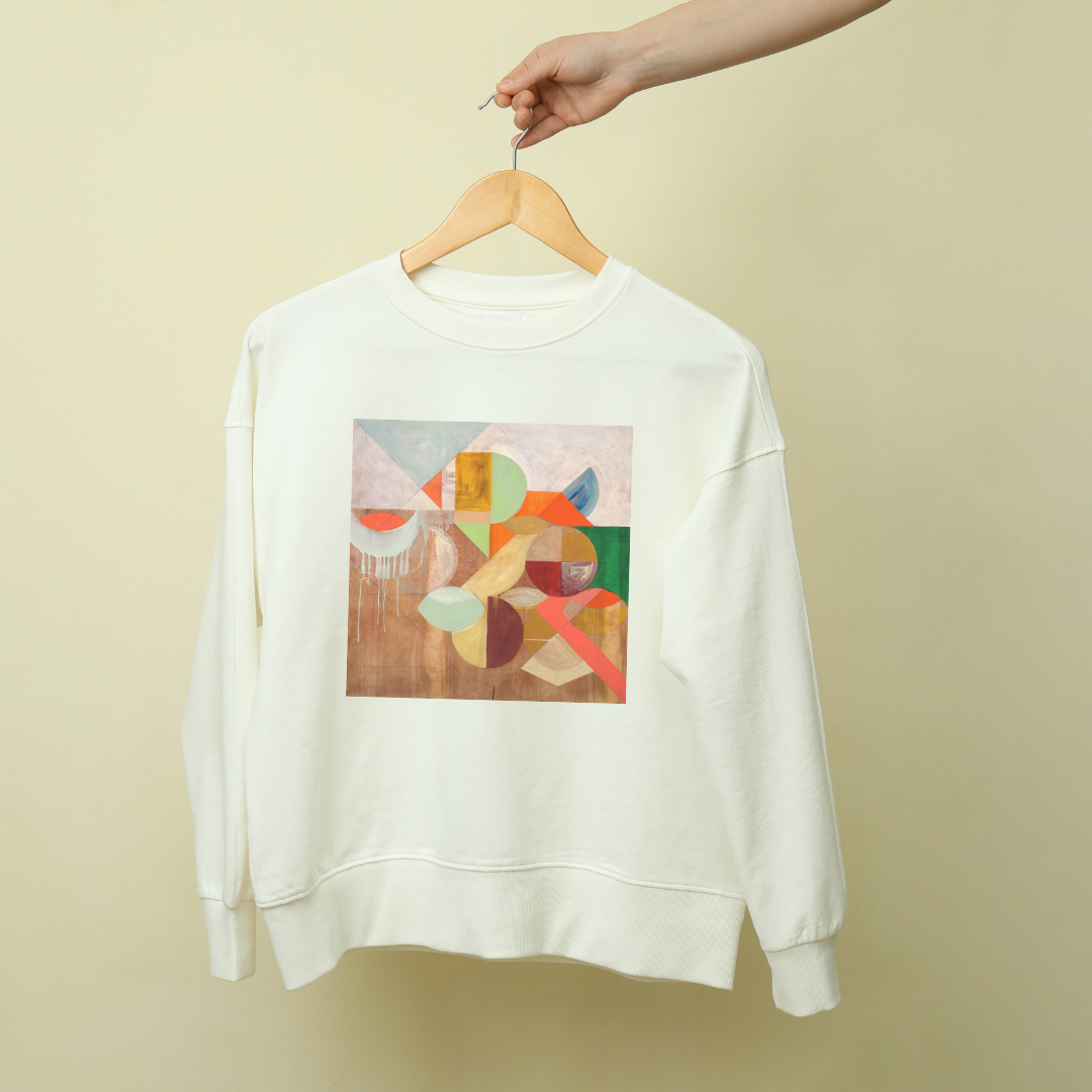 A white sweatshirt with a geometric pattern artwork on the front, displayed on a hanger against a beige background.