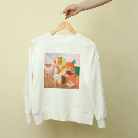 A white sweatshirt with a geometric pattern artwork on the front, displayed on a hanger against a beige background.
