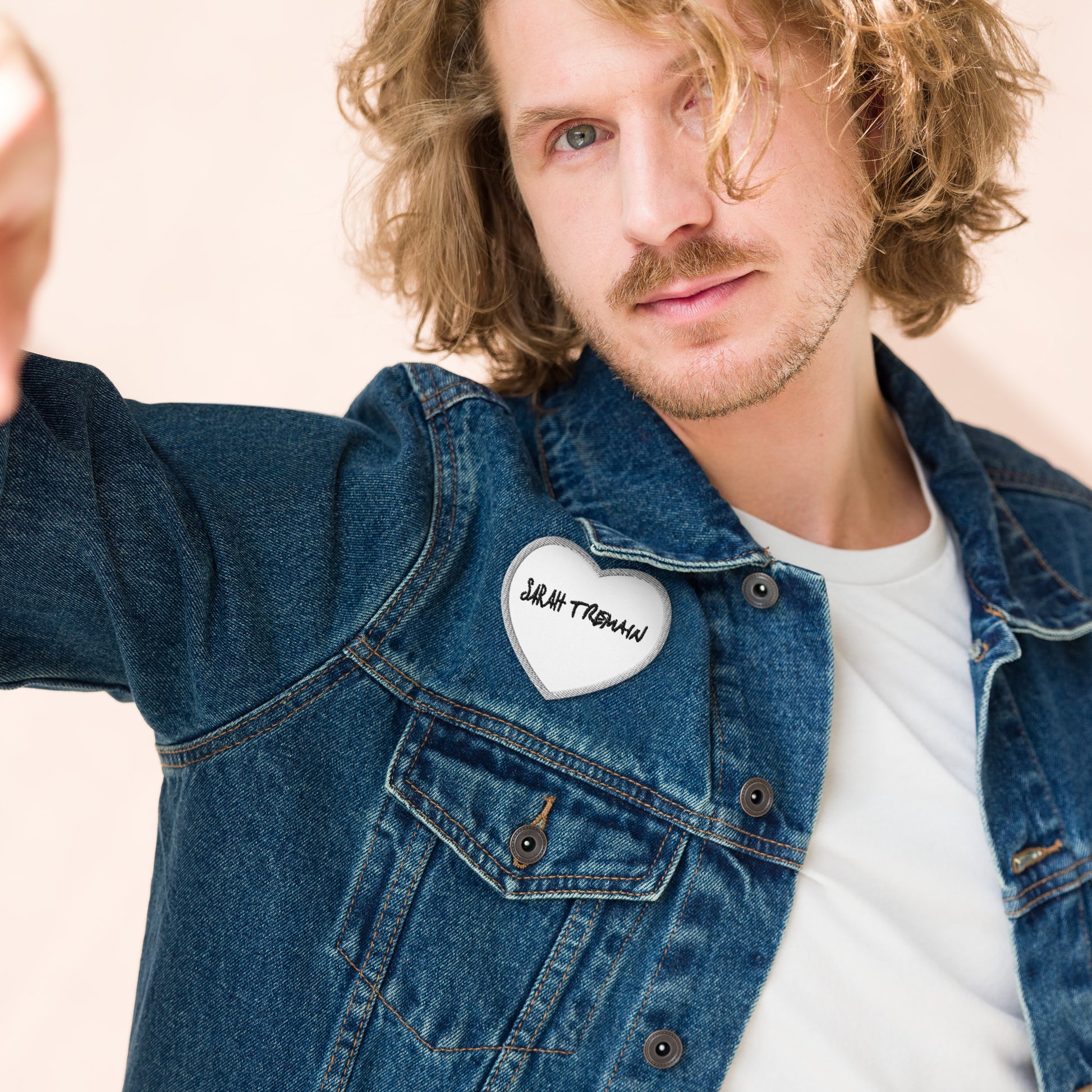 A white iron-on patch with the text 'SARAH TREMAIN' inside a heart-shaped design, shown on denim jacket on model
