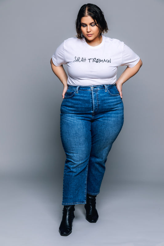 A woman wearing a white t-shirt with the text 'SARAH TREMAIN' on the front and blue jeans, paired with black boots.