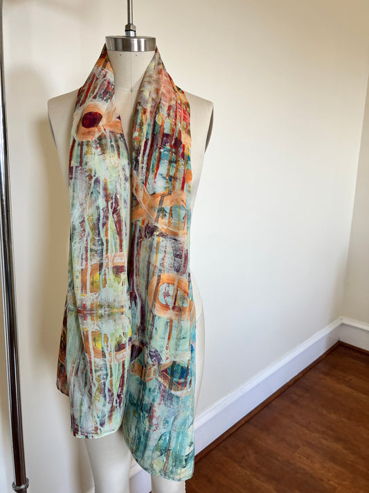 A large chiffon silk scarf with a vibrant, abstract multicolored print, displayed on a mannequin.