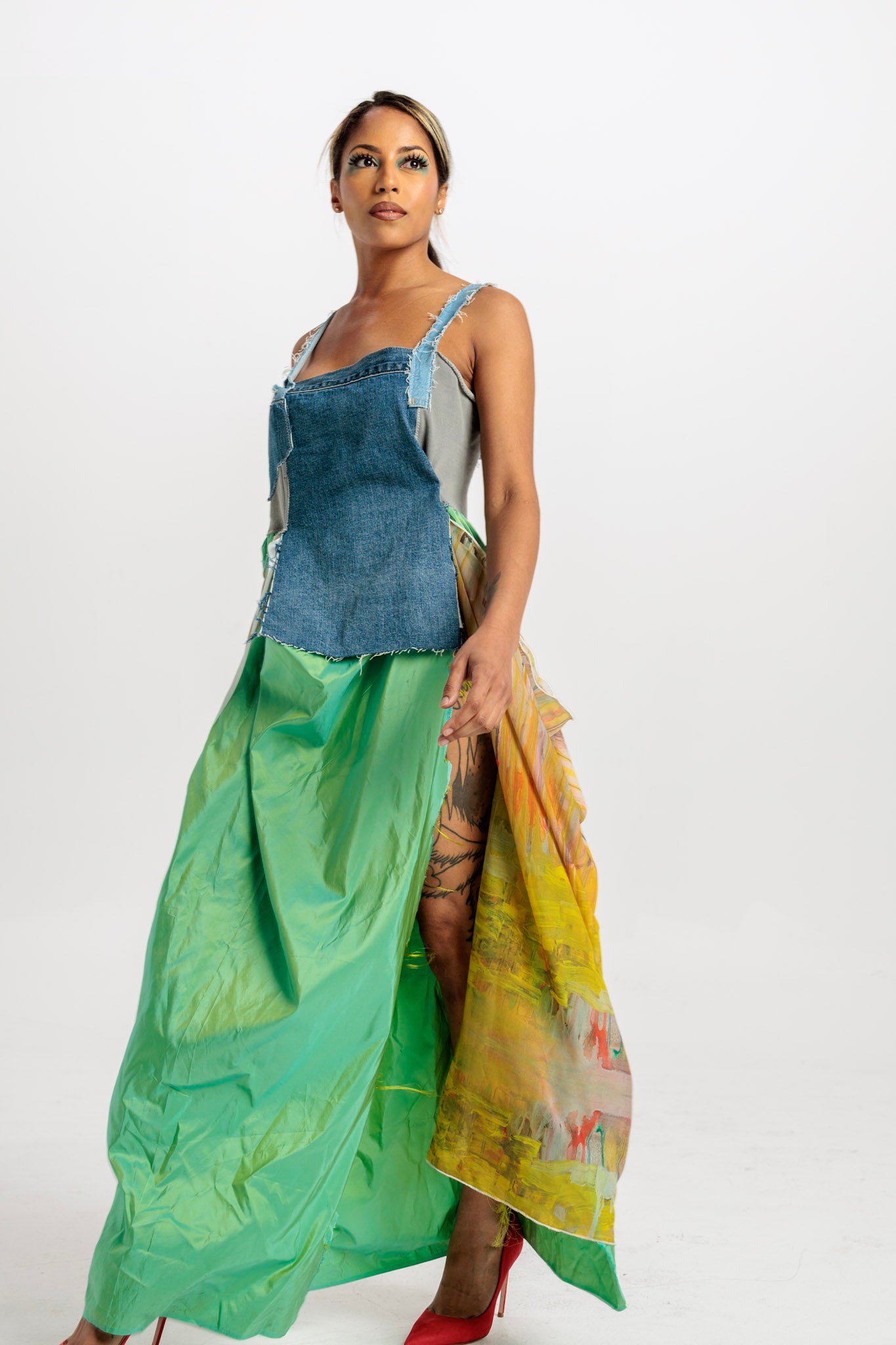 Woman wearing a green silk skirt panels made from reclaimed fabric, flowing from fitted denim bodice in front of a white background