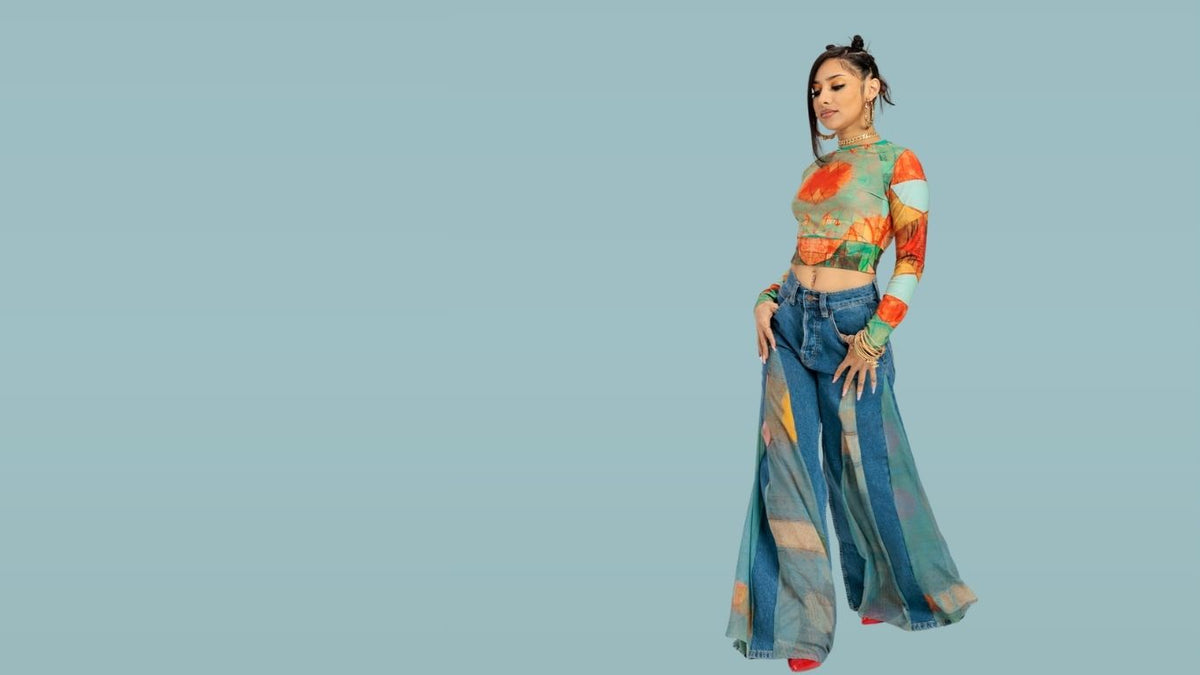 A woman modeling a matching two-piece outfit with a colorful abstract print, consisting of a long-sleeve crop top and wide-leg pants, set against a solid light blue background.